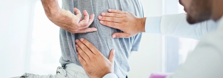 A chiropractor is performing a back exam on a man, focusing on the mid-back area.