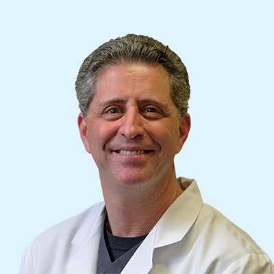 Gregory Kersh smiling with a light blue background.